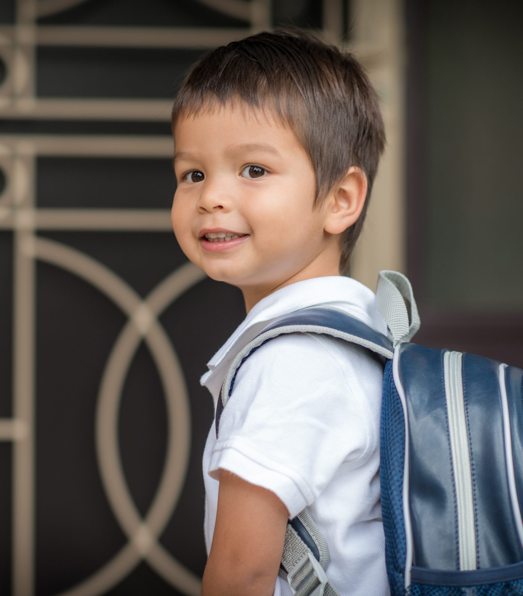 Cute 3 year old mixed race Asian Caucasian boy confidently leaves home for his first day at preschool